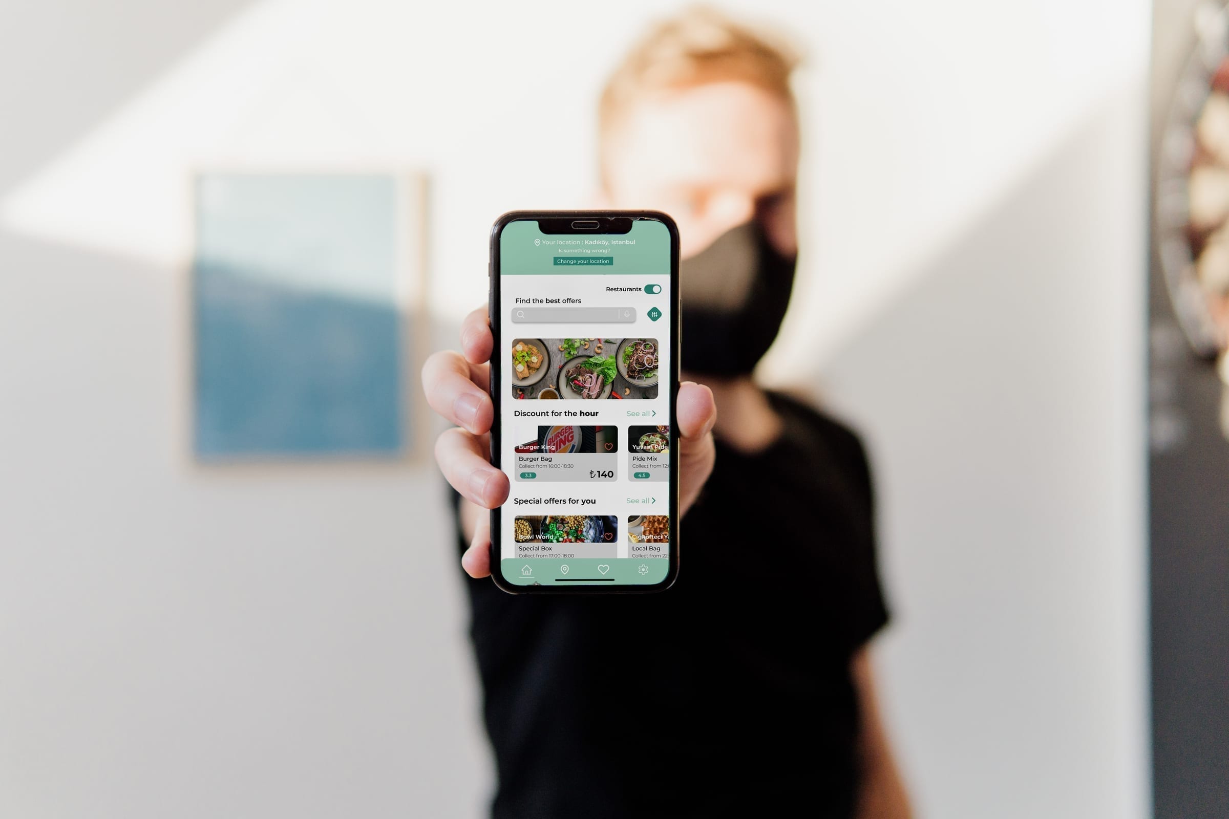 Person hält ein Smartphone mit dem GreenPlates+ Startbildschirm und Angebotslistings.